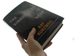 A person holding the book of Ray Kurzweil. The title of the book is: "The singularity is near". Iemand houdt het boek van Ray Kurzweil vast. De titel van het boek is: "De singulariteit is nabij".